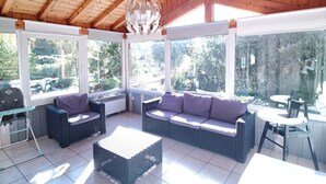 A covered outdoor seating area with wicker furniture and large windows.