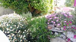 En have med forskellige blomster og buske, en stenvæg og et stort træ.