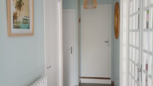 En gang med lyseblå vægge, hvide døre, en radiator og en hængende lampe.