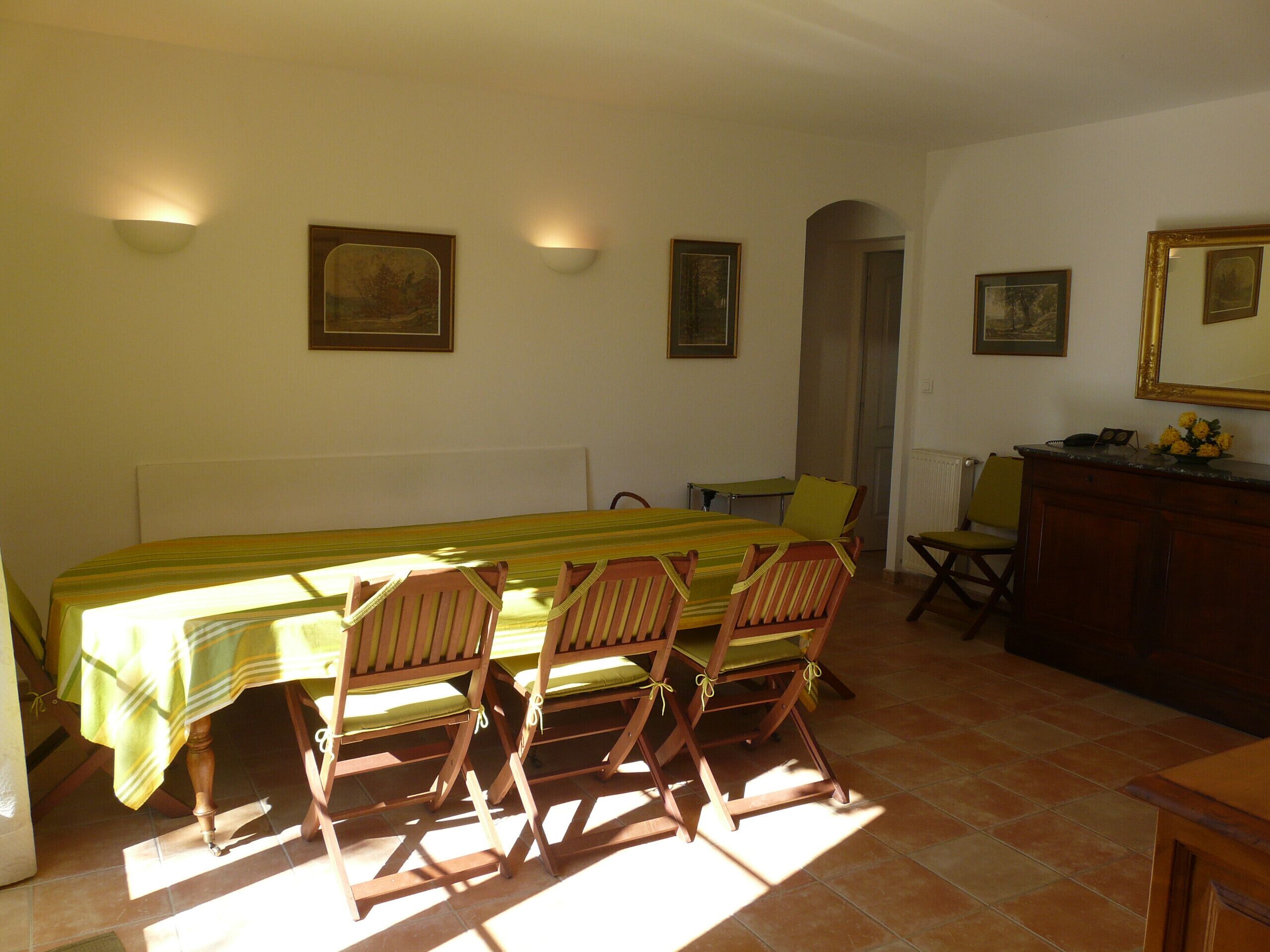 A dining area with a long table, wooden chairs, and wall-mounted light fixtures.