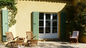 An outdoor seating area with wooden chairs and a table, a large window with shutters, and a small chair with a floral pattern. - Vacation rental with heated  pool Mouries LS1-140 (Mouriès)