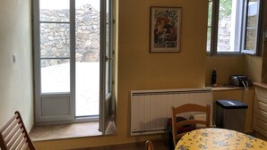 A room with a stone wall outside, a radiator, a wooden chair, a table with a floral tablecloth, and a poster on the wall. - Corsican house perfect for hot weather between Monte Cinto and Calacuccia Lake  (LOZZI)