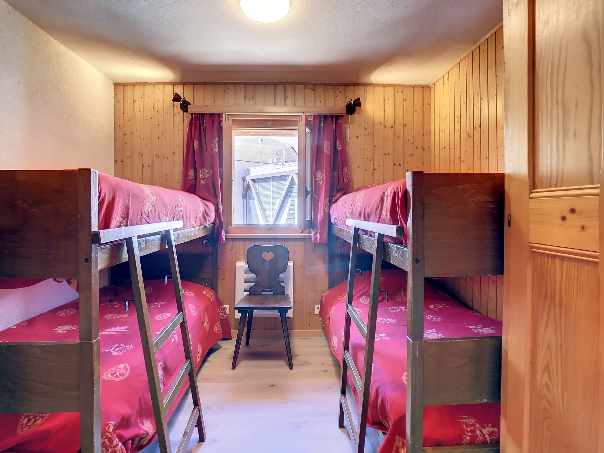 Une chambre de dortoir avec deux lits superposés, une chaise en bois et une fenêtre avec des rideaux.