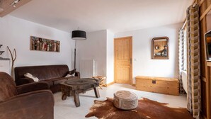 Ein Wohnzimmer mit einem braunen Ledersofa, einem Holztisch, einem Kuhfellteppich, einer Holzkiste und einem Bild an der Wand.