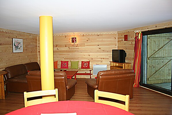 Un interior de madera con un conjunto de sofás, un televisor y un ventanal con cortinas.