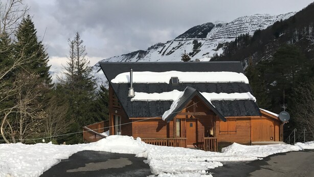 Een houten hut met een schuin dak, omgeven door besneeuwde bergen en bomen.