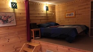 Een gezellig houten kamer met een bed, een tafeltje, een verwarming en een schilderij aan de muur.
