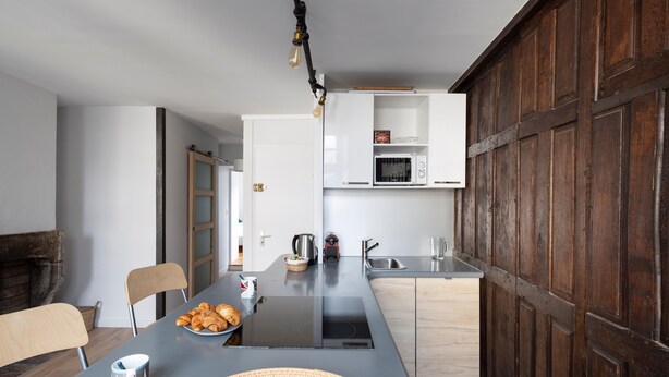 A modern kitchen with a central island, built-in microwave, and wooden cabinets. - LE CORSAIRE - Petit cocon dans l'Intra-Muros (Saint-Malo)
