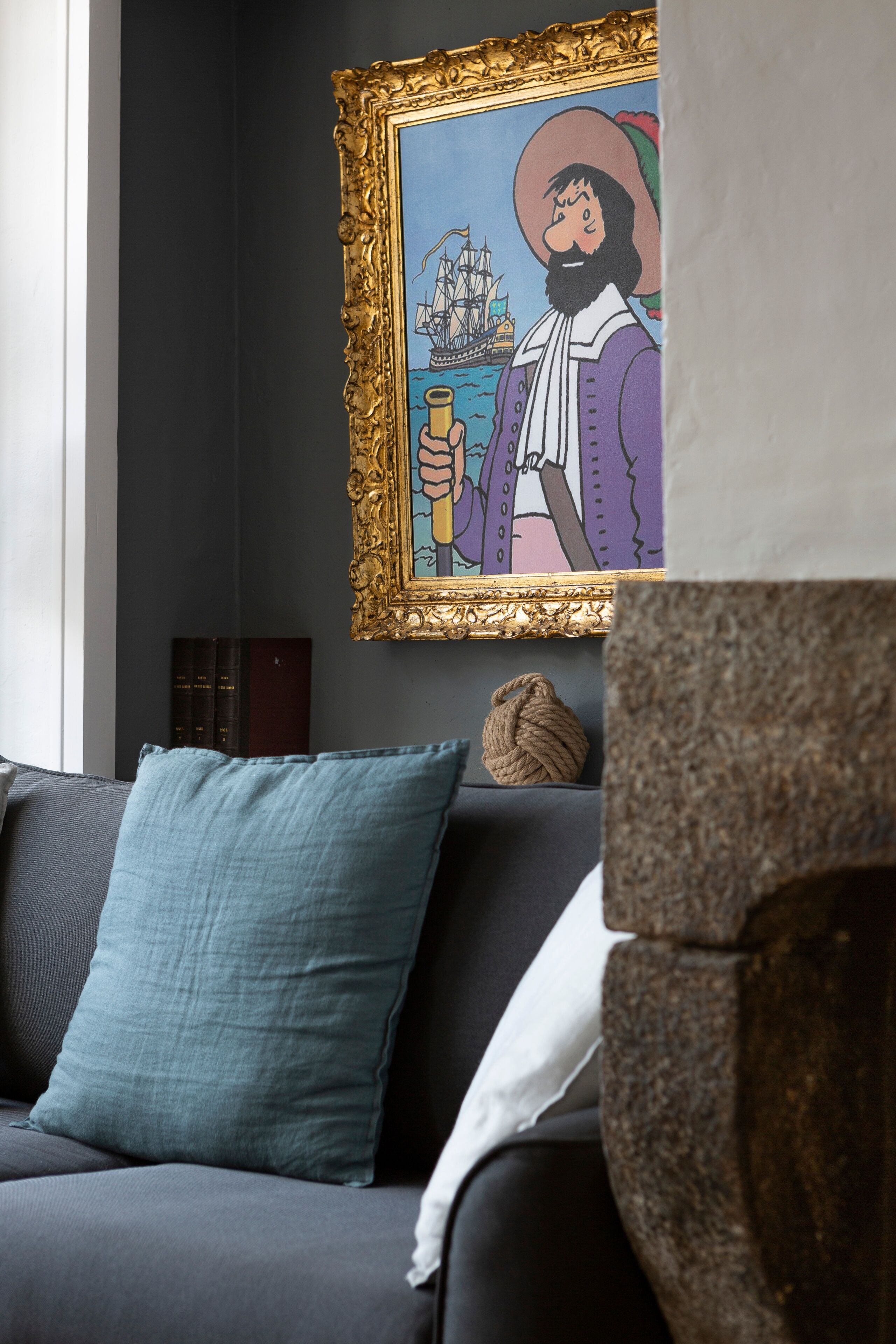 A room with a dark-colored sofa, a framed artwork depicting a historical scene, and a textured stone sculpture.