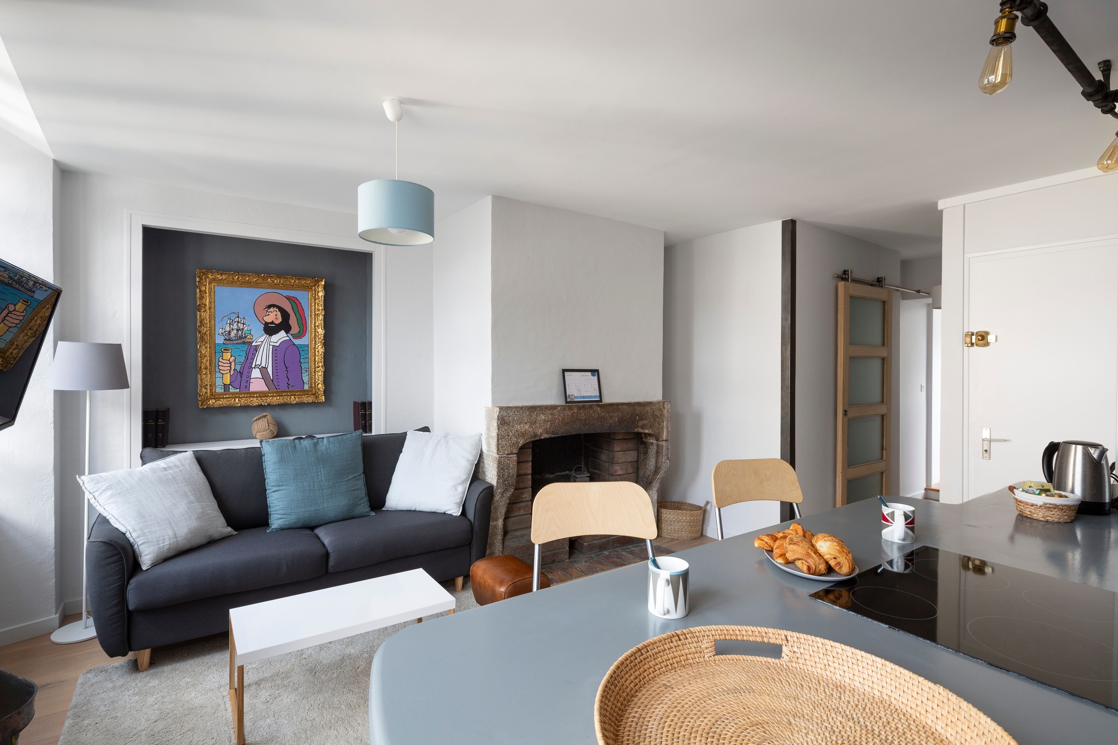 Uma sala de estar moderna com um sofá, uma mesa de jantar, uma lareira e um quadro na parede.