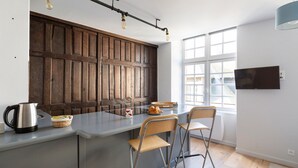 A modern kitchen with a large island, wooden panel wall, and a TV mounted on the wall. - LE CORSAIRE - Petit cocon dans l'Intra-Muros (Saint-Malo)