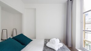 A hotel room with a bed, teal pillows, a gray patterned bed runner, and a window with curtains. - LE CORSAIRE - Petit cocon dans l'Intra-Muros (Saint-Malo)