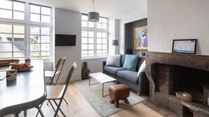 A modern living room with a fireplace, a dining area with a table and chairs, and a sofa with cushions. - LE CORSAIRE - Petit cocon dans l'Intra-Muros (Saint-Malo)