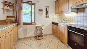 Una cocina con armarios de madera, lavavajillas, ventana con cortina y salpicadero de azulejos.