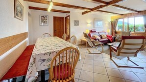 Comedor con mesa lista para cuatro, sillas de madera, sofá y vistas al exterior a través de amplios ventanales.