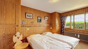 Una habitación con paneles de madera, una cama, una silla y una ventana que da a zonas verdes.