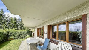 Un patio al aire libre con mesa y dos sillas, una sección cubierta y vistas de la vegetación circundante.