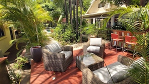 A covered outdoor patio with wicker furniture, a red floor, and lush greenery. - Superb villa with heated swimming pool and jacuzzi in lush greenery (Saint-Pierre)