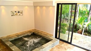 A spa area with a hot tub, stone tiles, and a glass door leading to a garden. - Superb villa with heated swimming pool and jacuzzi in lush greenery (Saint-Pierre)