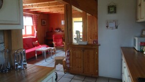 Un accogliente interno di una baita con zona pranzo in legno, un divano rosso e una cucina con pensili e forno a microonde.