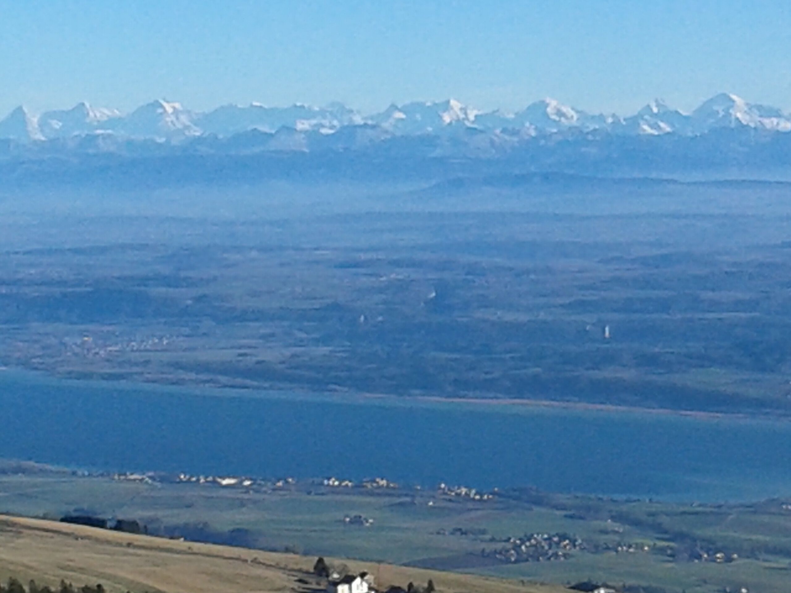 A panoramic view of a coastal landscape with a town in the foreground and snow-capped mountains in the background.