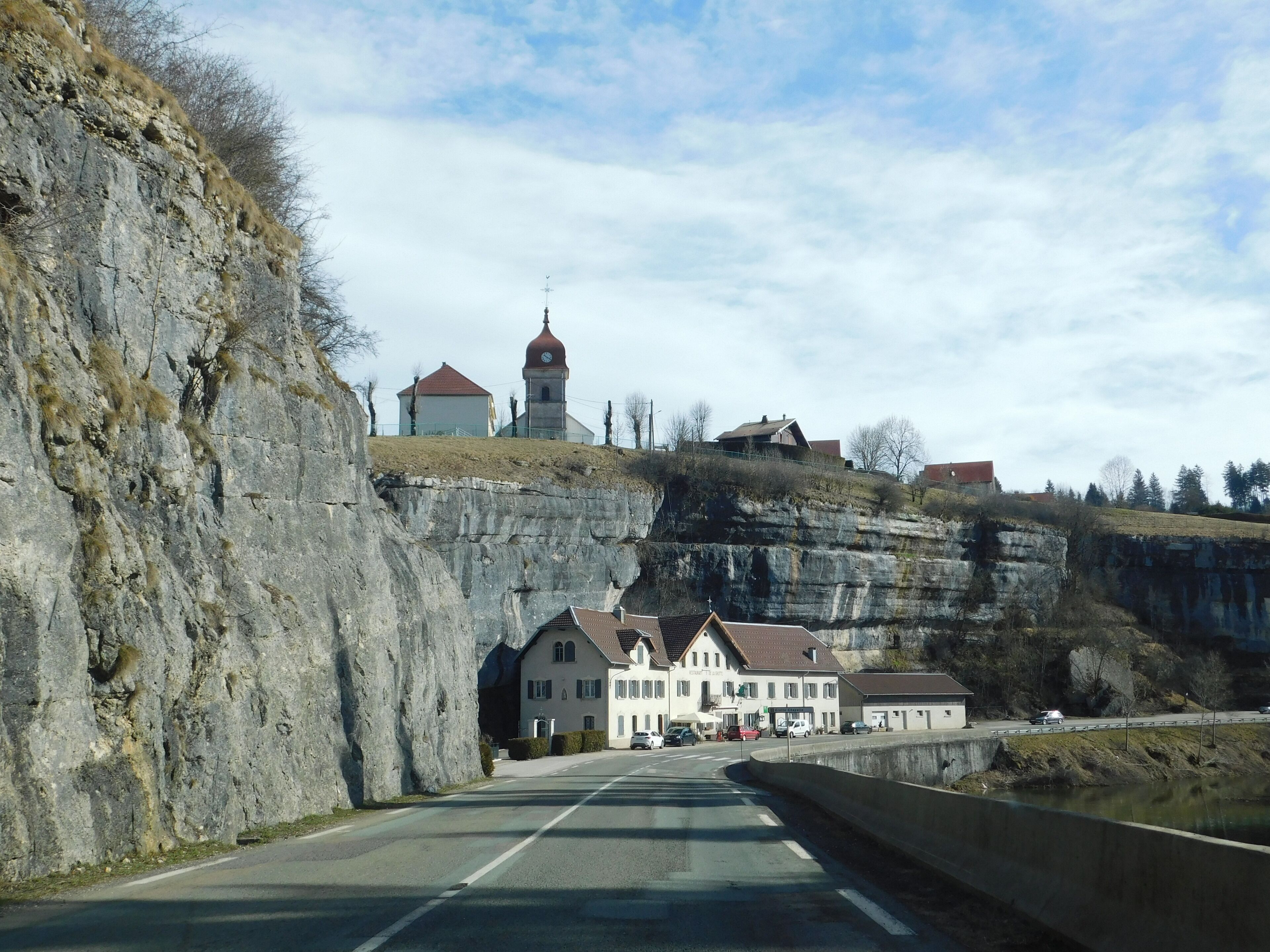 A road passing through a valley with a large cliff on one side and a building with a red roof on the other.
