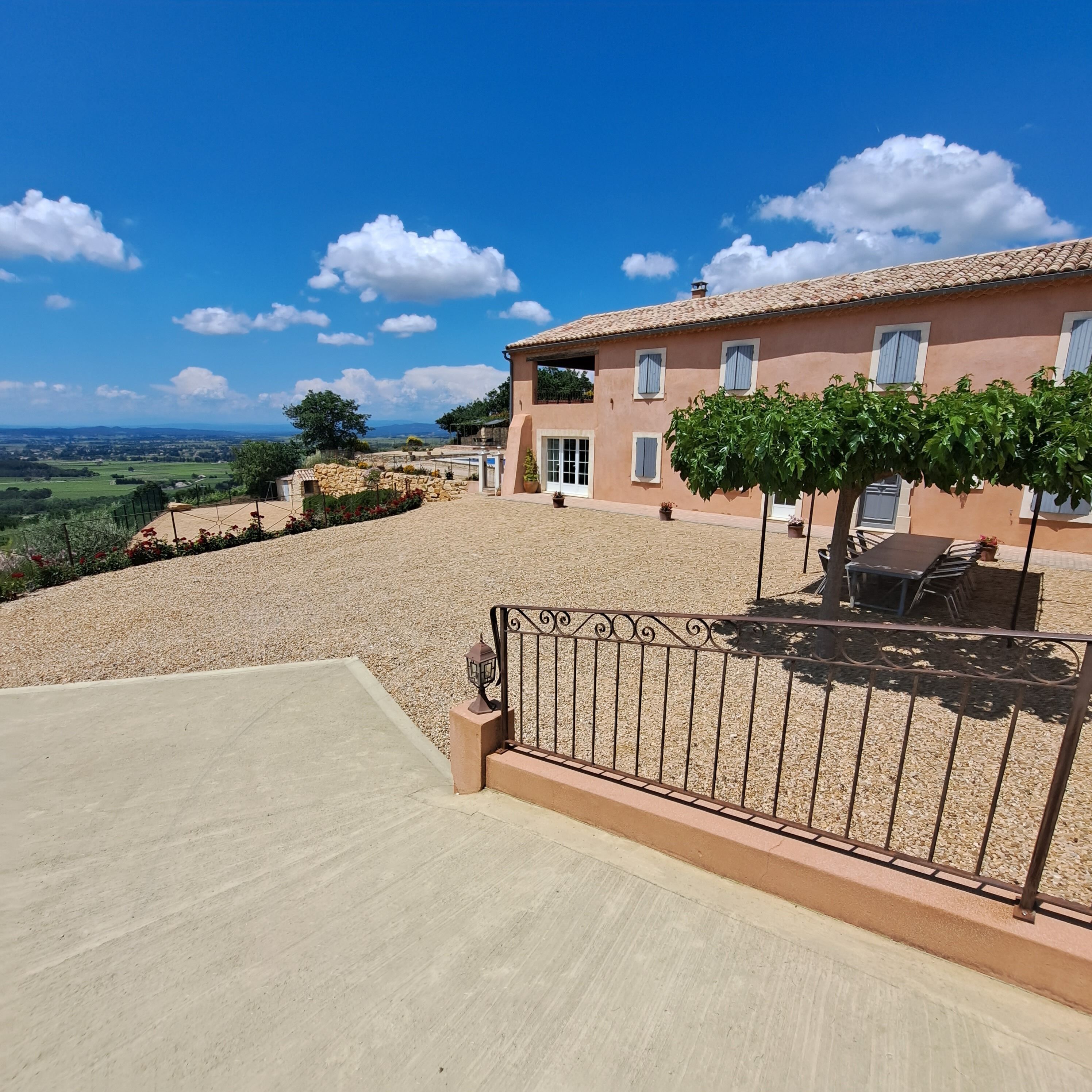 A villa with a stone terrace, a dining area, and a view of the countryside.