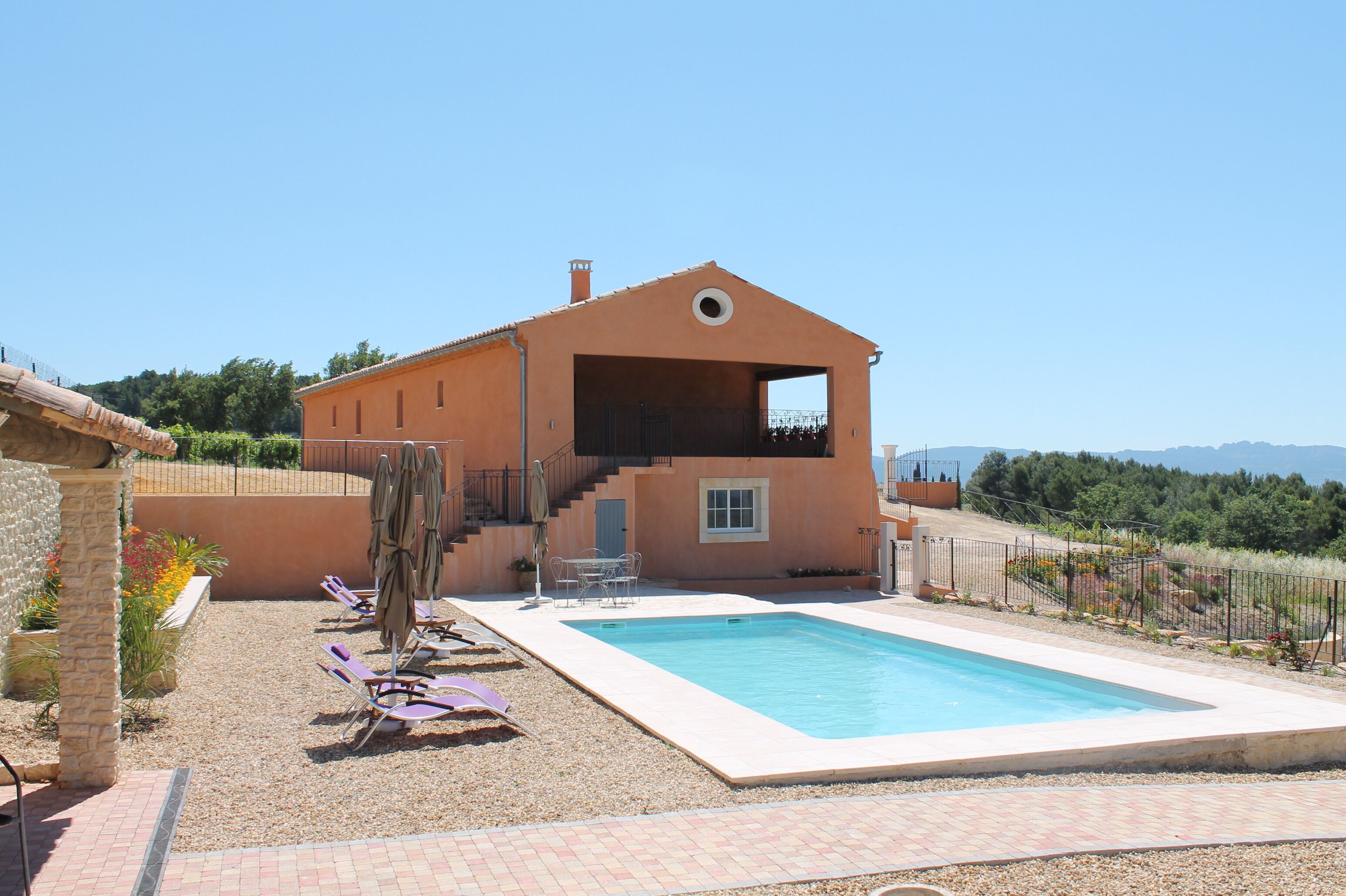 A two-story house with a swimming pool, outdoor seating, and a view of the surrounding landscape.