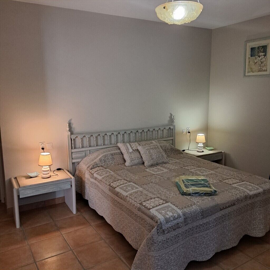 A bedroom with a bed, two bedside tables with lamps, a ceiling light fixture, and a framed picture on the wall.