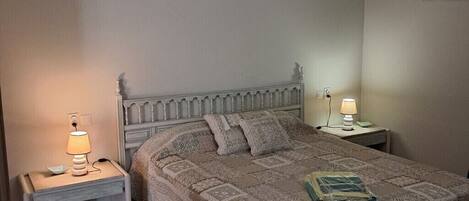 A bedroom with a bed, two bedside tables with lamps, a ceiling light fixture, and a framed picture on the wall.