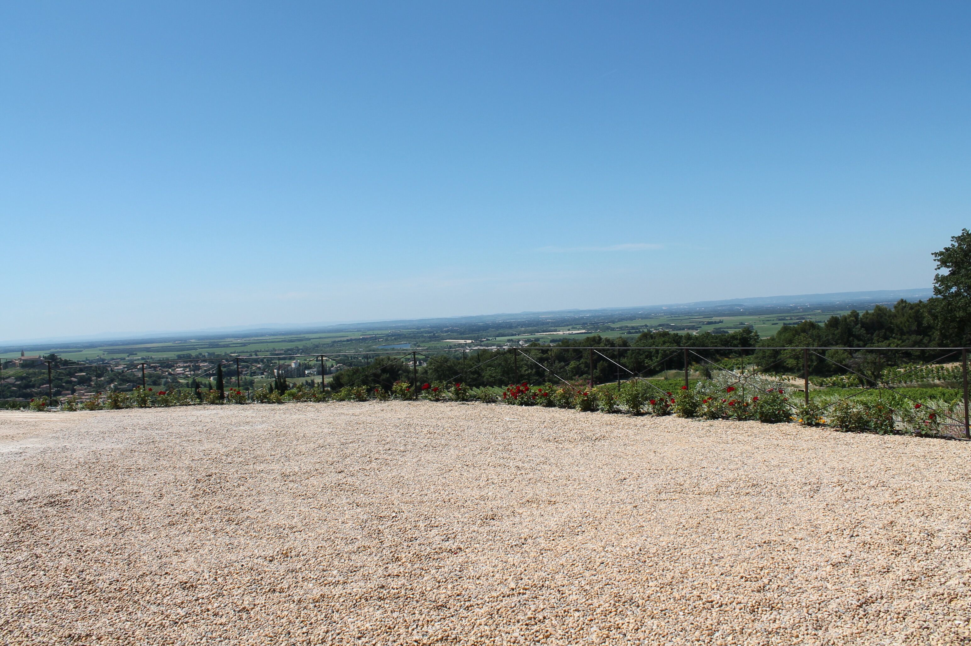 A gravel area with a fence and a view of a distant town.
