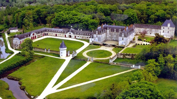 An aerial view of a large, historic estate with a central courtyard, multiple buildings, and extensive green lawns.