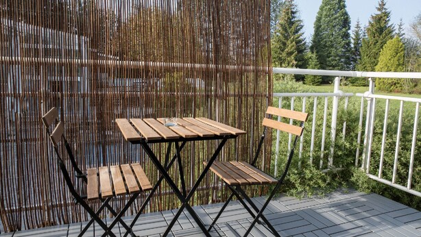 Um deck de madeira com mesa e cadeiras, um corrimão branco e uma cerca de bambu.