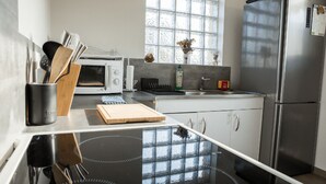 Uma cozinha moderna com bancada preta, forno branco, geladeira de aço inoxidável e janela com vista para árvores.