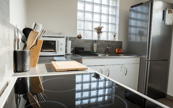 A modern kitchen with a black countertop, a white oven, a stainless steel refrigerator, and a window with a view of trees.