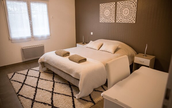 Un dormitorio ordenado con una cama, dos mesitas de noche, un radiador y una alfombra estampada.