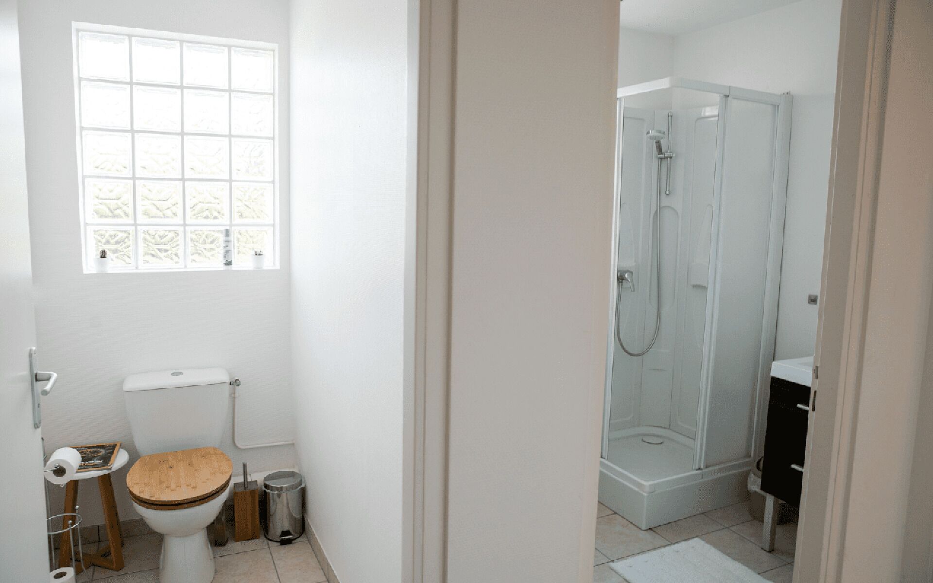 A bathroom with a toilet, a window, a shower, and a sink.