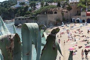 Une plage où l’on voit des gens se prélasser au soleil et se promener, un mur de pierre et des bâtiments en arrière-plan.