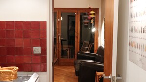 A room with a red tiled wall, a wooden floor, a black leather sofa, and a wicker basket. - 5 minutes from the beach, a charming apartment in a beautiful residence.... (CALELLA DE PALAFRUGELL)