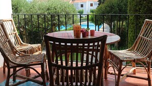 A round table with wicker chairs on a balcony overlooking a swimming pool and greenery. - 5 minutes from the beach, a charming apartment in a beautiful residence.... (CALELLA DE PALAFRUGELL)