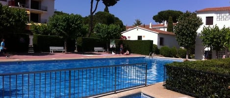 Una piscina con bordo piastrellato, circondata da vegetazione e edifici.