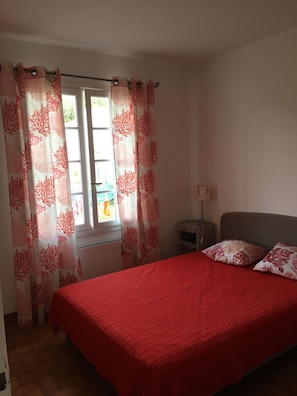 A bedroom with a bed, a nightstand, and a window with curtains.