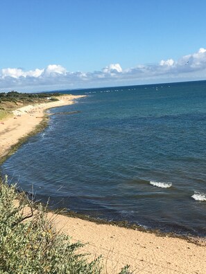 Ein Strand mit blauem Himmel, ruhiger See und Booten in der Ferne.
