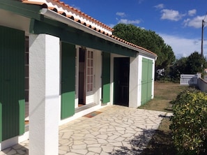 A house with a stone-paved entrance, green shutters, and a tiled roof.