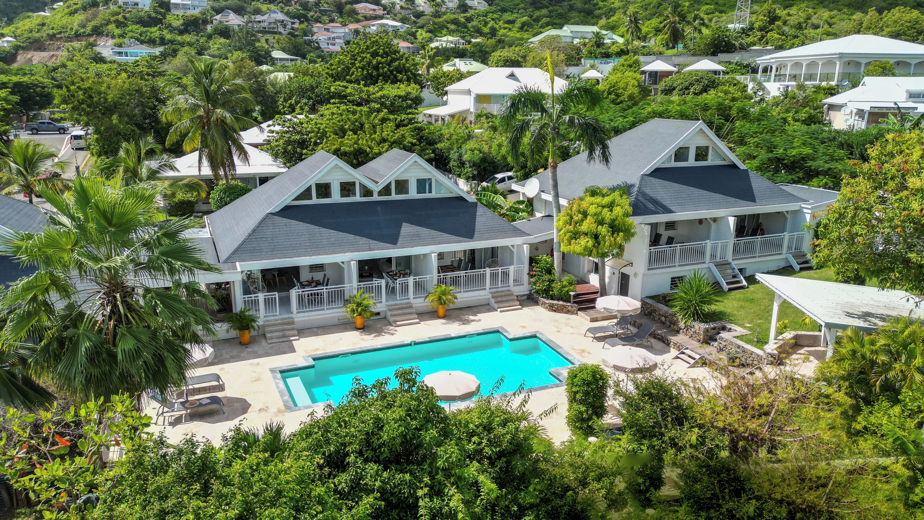 A large house with a swimming pool, surrounded by lush greenery and other houses.