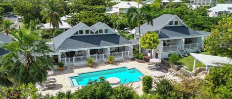 A large house with a swimming pool, surrounded by lush greenery and other houses.