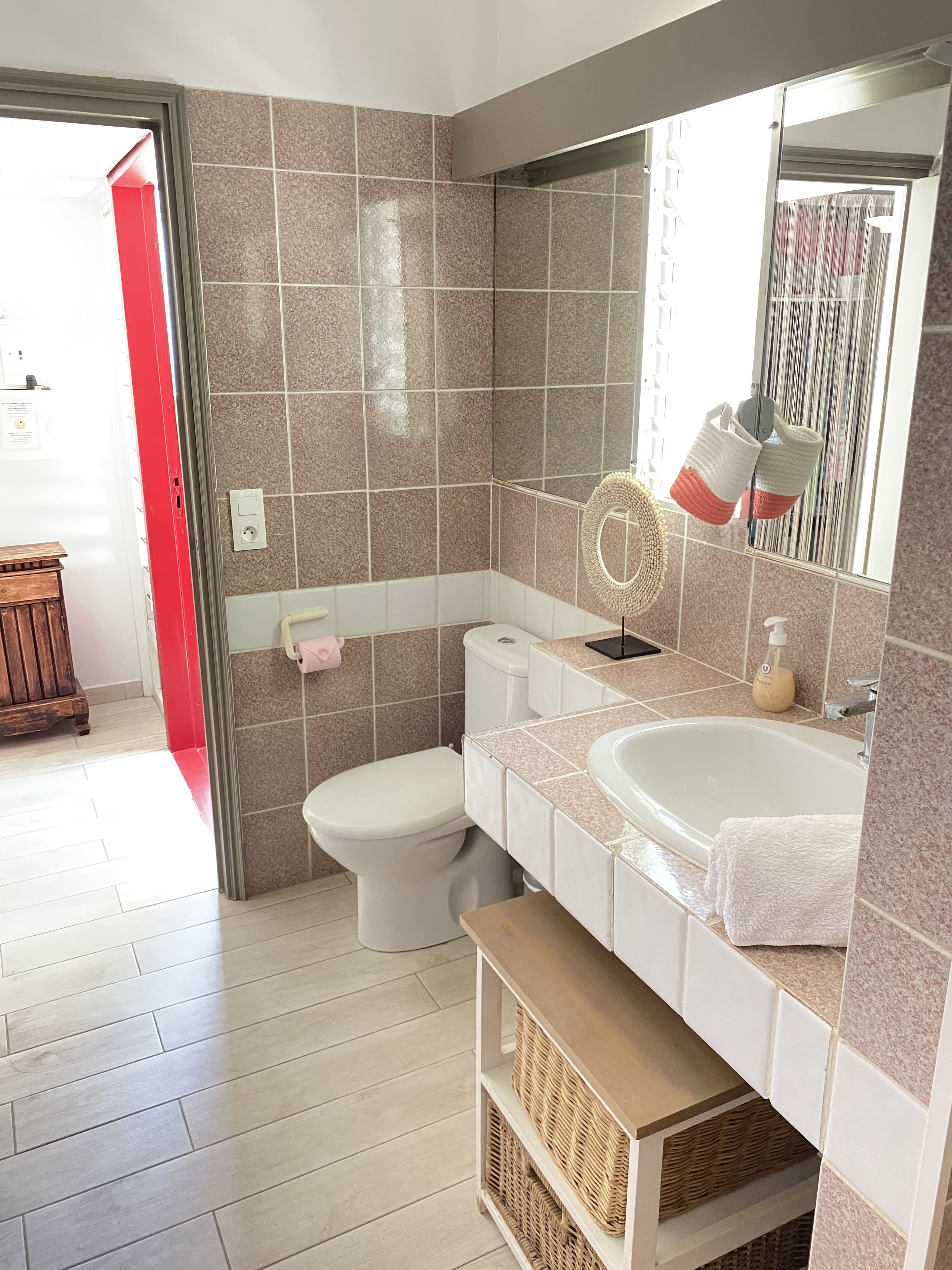 A bathroom with a toilet, sink, and mirror. There is a red door leading to another room.
