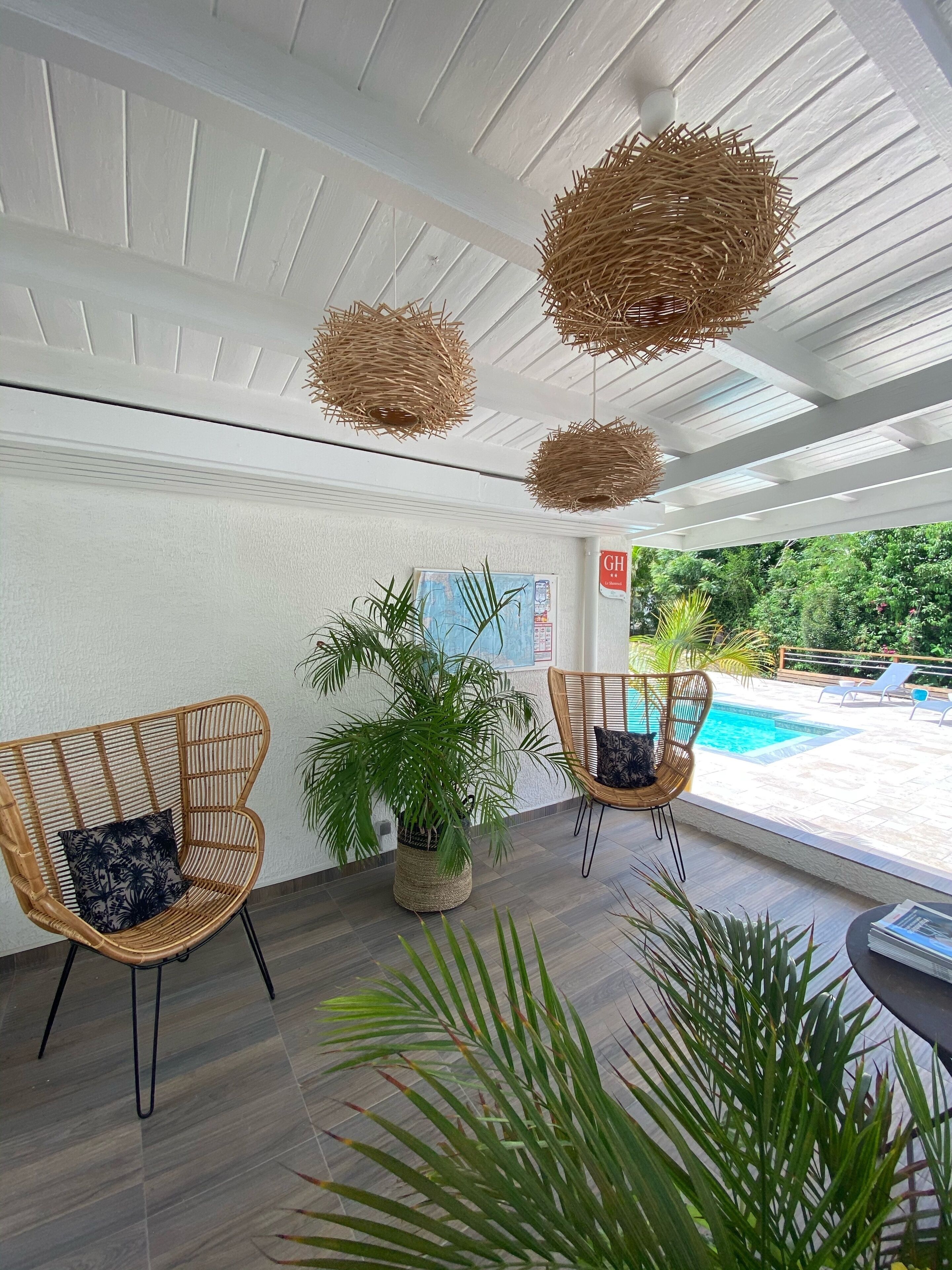 A modern indoor area with wicker chairs, potted plants, and a view of an outdoor swimming pool.