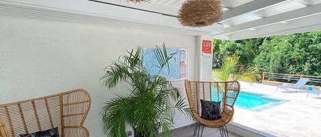 A modern indoor area with wicker chairs, potted plants, and a view of an outdoor swimming pool.