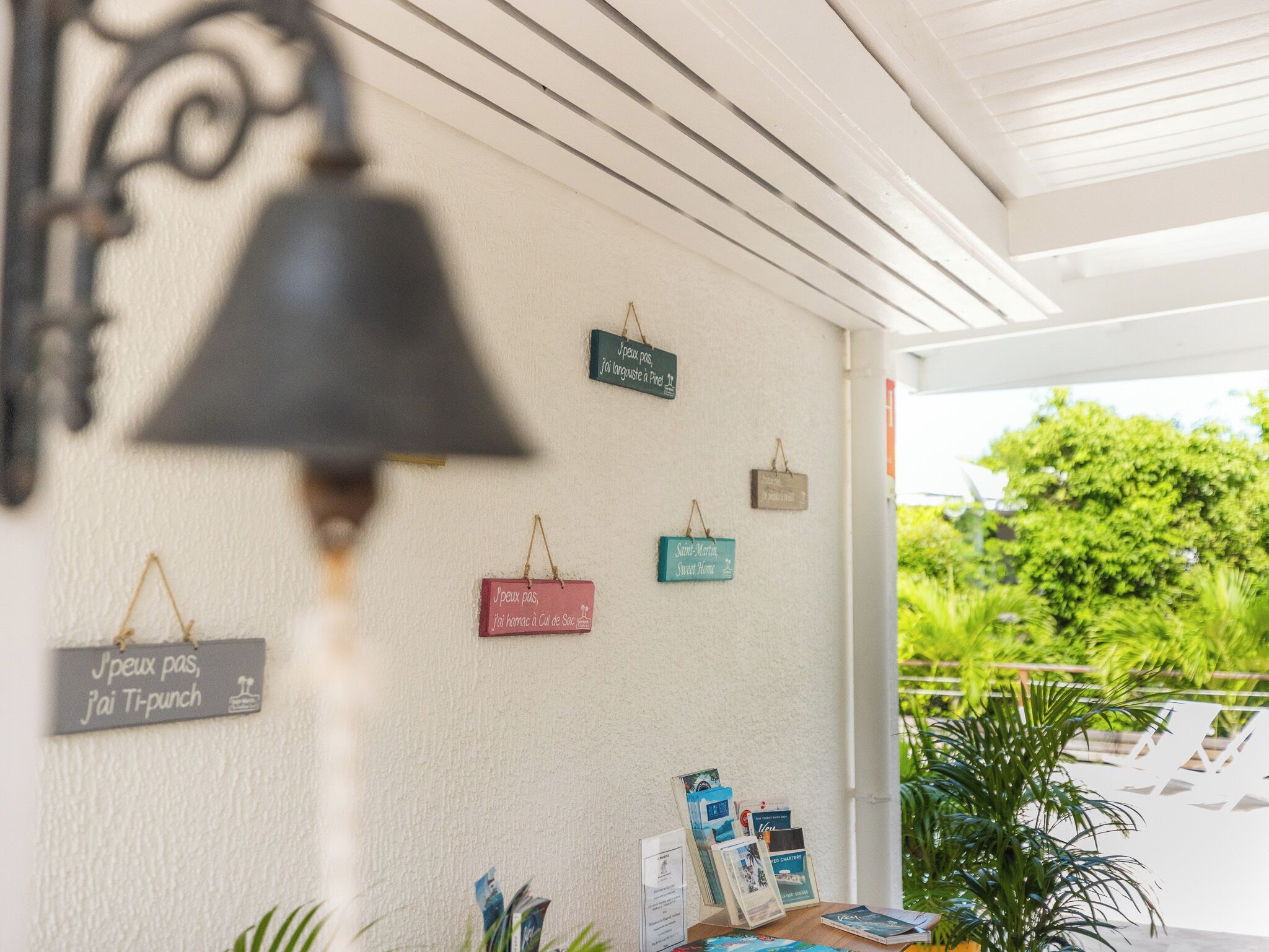 Una pared con letreros colgantes y una campana, una mesa con libros y una carta, y vista a zonas verdes al exterior.
